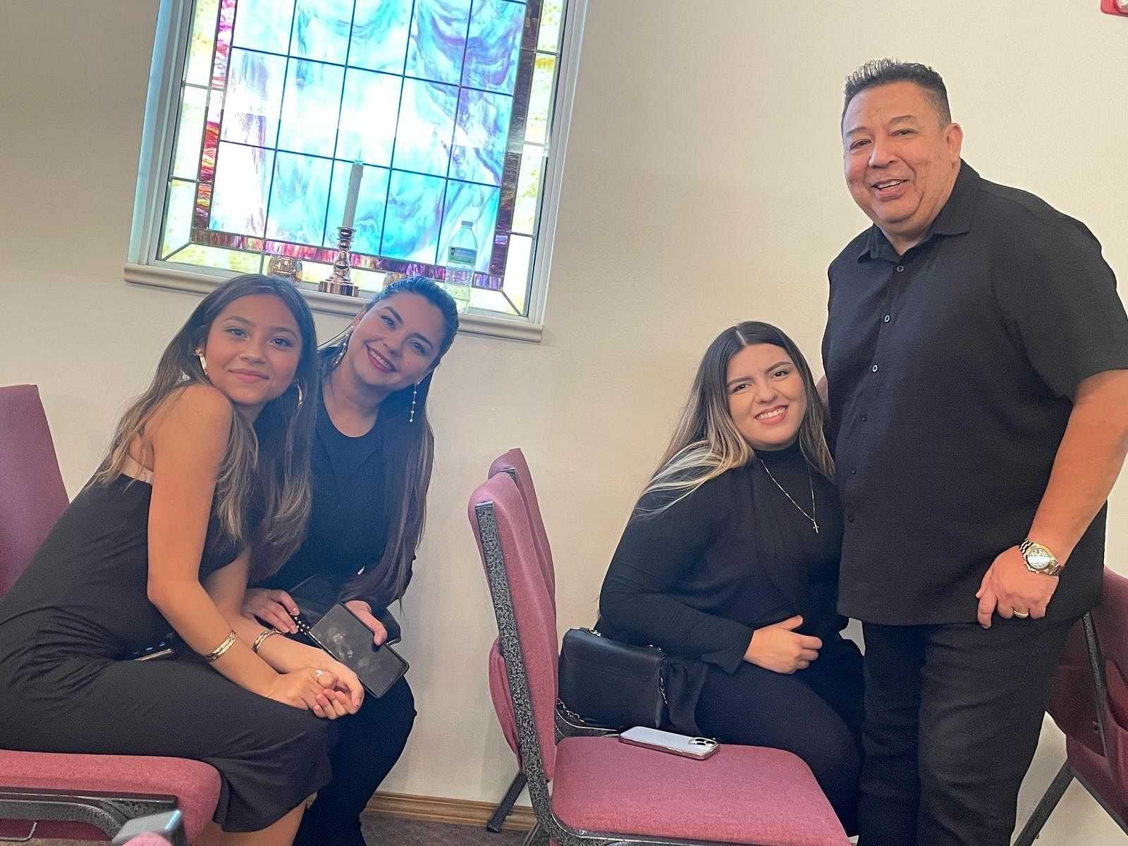 Four people smiling and sitting in a church with a colorful stained-glass window behind them.