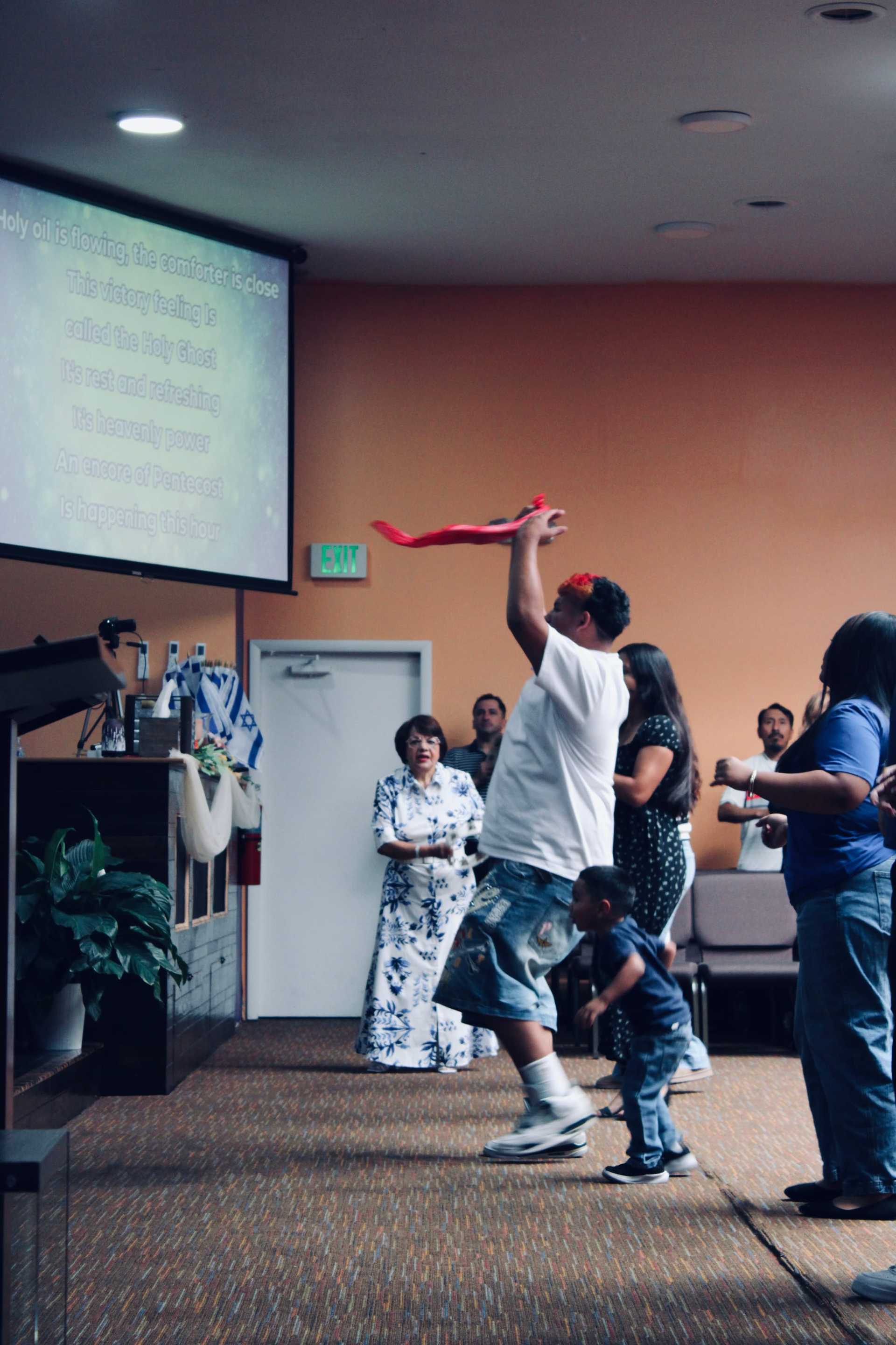 Worshippers in a church service, one man waving a red ribbon enthusiastically.