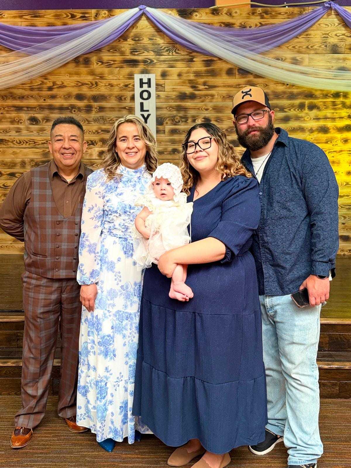 Family posing together at a celebration, with baby dressed in white.