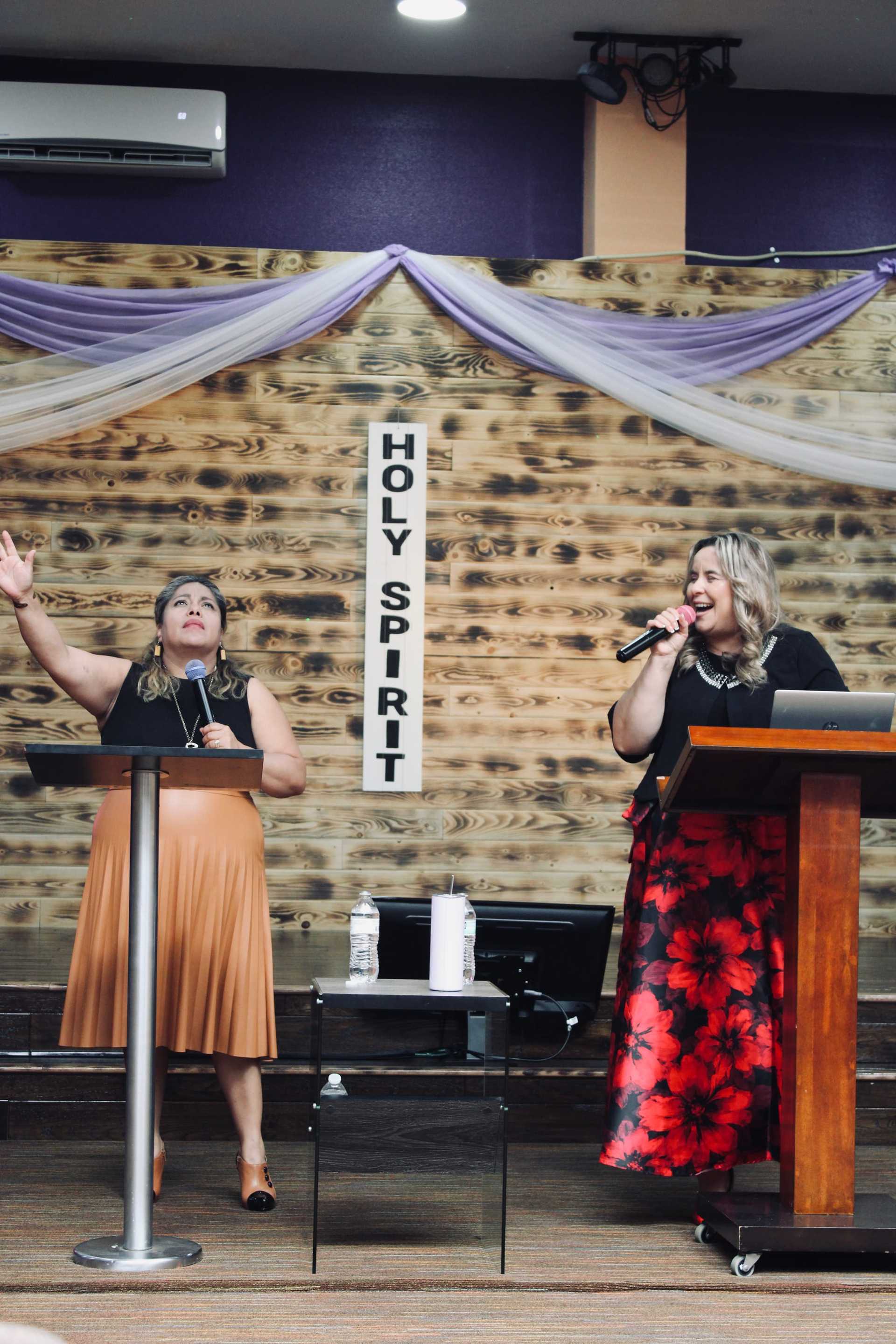 Two women speaking on stage with "Holy Spirit" sign in background.