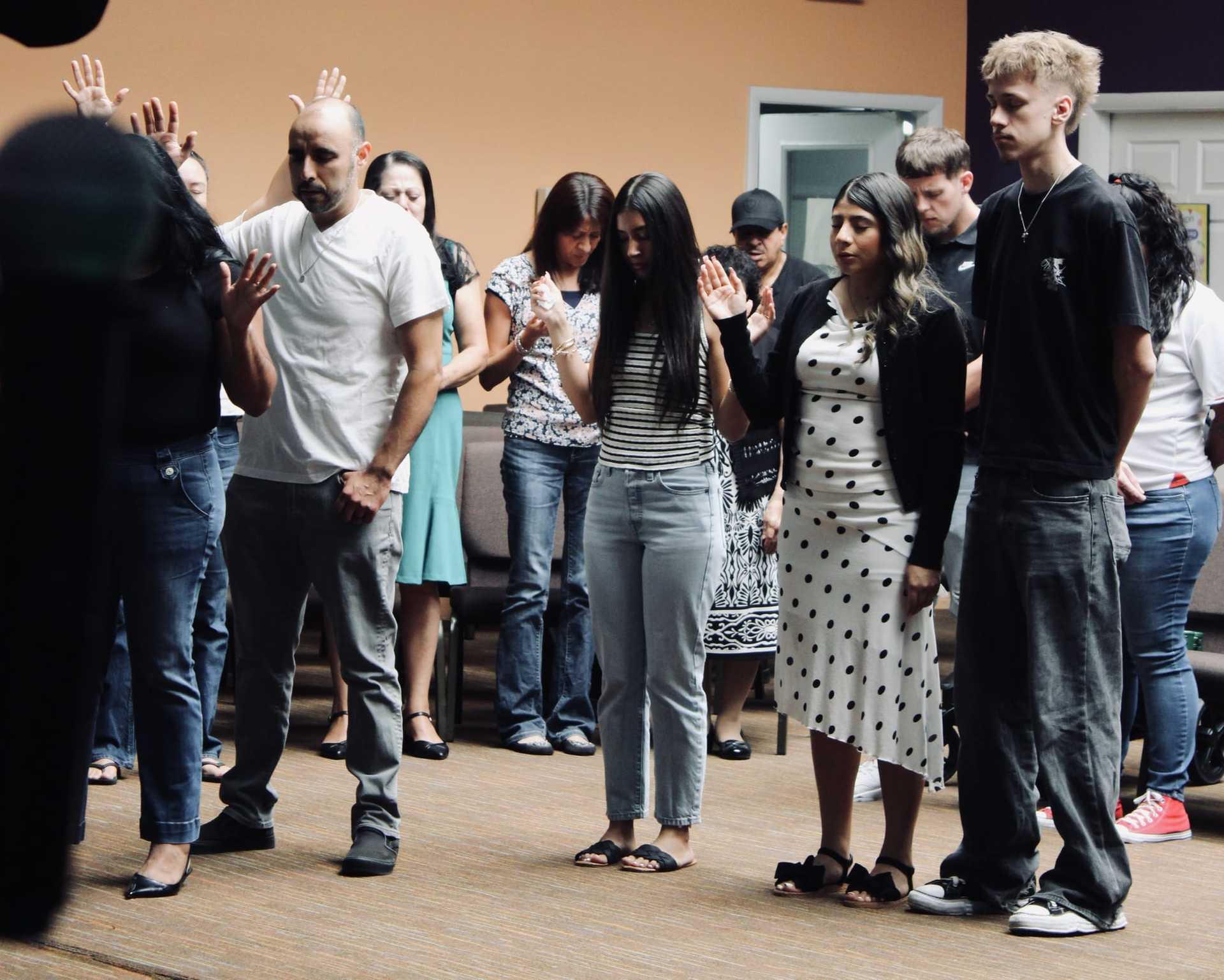 People standing with raised hands in a group gathering indoors.