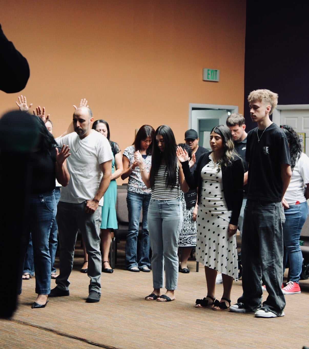 A group of people stands indoors, some with their hands raised, appearing attentive.