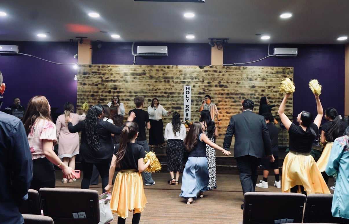 Group of people in a room singing and dancing with raised hands.